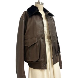 Puede incluir: Chaqueta bomber de cuero marr&oacute;n con cuello de piel sint&eacute;tica negra. La chaqueta tiene dos bolsillos delanteros y un dobladillo acanalado. La chaqueta se exhibe en un maniqu&iacute;.
