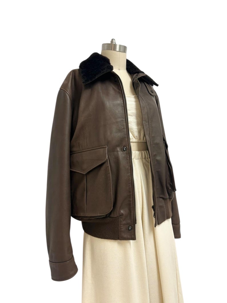 Puede incluir: Chaqueta bomber de cuero marr&oacute;n con cuello de piel sint&eacute;tica negra. La chaqueta tiene dos bolsillos delanteros y un dobladillo acanalado. La chaqueta se exhibe en un maniqu&iacute;.