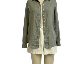 May include: A long-sleeved, olive green button-down shirt paired with cream-colored shorts. The shirt has a classic collar and button closure. The shorts are a neutral color, creating a simple, coordinated outfit. The clothing is displayed on a mannequin.