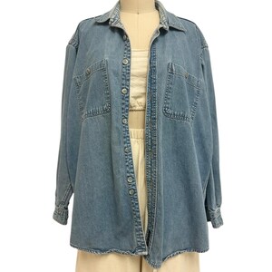 Op de afbeelding: Een lichtblauw spijkeroverhemd met lange mouwen, twee borstzakken en een knoopsluiting. Het overhemd wordt getoond op een mannequin, gecombineerd met een cr&egrave;mekleurige top en broek. Het overhemd heeft een klassieke kraag en manchetten.