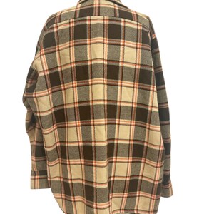 May include: A plaid button-down shirt in a neutral color palette. The shirt features a brown, tan, and peach plaid pattern. The long-sleeved shirt has a classic collar and buttoned cuffs. The back of the shirt is visible, showcasing the pattern's symmetry.
