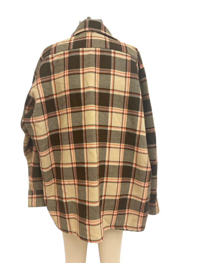 May include: A plaid button-down shirt in a neutral color palette. The shirt features a brown, tan, and peach plaid pattern. The long-sleeved shirt has a classic collar and buttoned cuffs. The back of the shirt is visible, showcasing the pattern's symmetry.