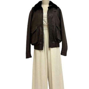 Puede incluir: Chaqueta de cuero marr&oacute;n con cuello de piel negra y dos bolsillos delanteros. La chaqueta se combina con un top corto color crema y pantalones de pernera ancha. El conjunto se exhibe en un maniqu&iacute;.