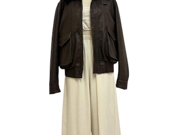 May include: A brown leather jacket with a black fur collar and two front pockets. The jacket is paired with a cream-colored crop top and wide-leg pants. The outfit is displayed on a mannequin.