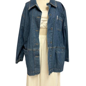 May include: A blue denim jacket with a button-up front and a single chest pocket. The jacket has a relaxed fit and long sleeves.