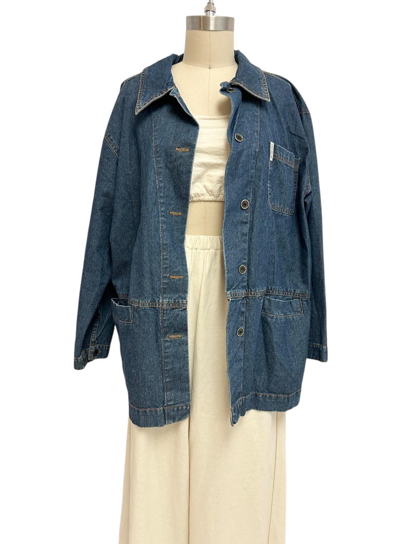 May include: A blue denim jacket with a button-up front and a single chest pocket. The jacket has a relaxed fit and long sleeves.