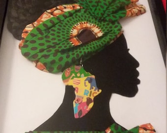 Könnte beinhalten: Eine schwarze Silhouette einer Person, die einen grün-orangen gemusterten Kopftuch und ein passendes Kleid trägt. Die Person trägt einen großen, bunten Ohrring in Form des afrikanischen Kontinents.