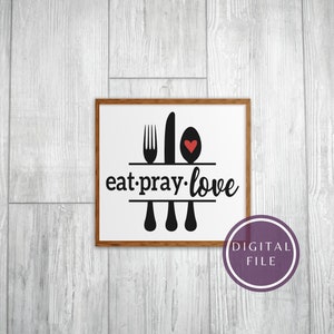 May include: A white framed print with black text that reads "eat.pray.love" and a black silhouette of a fork, knife, and spoon with a red heart in the spoon.