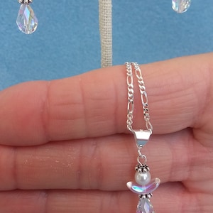 May include: A silver chain necklace with a pendant featuring a small white pearl and a crystal angel with iridescent wings.
