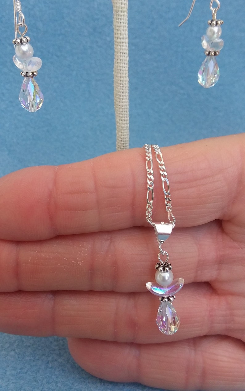 May include: A silver chain necklace with a pendant featuring a small white pearl and a crystal angel with iridescent wings.