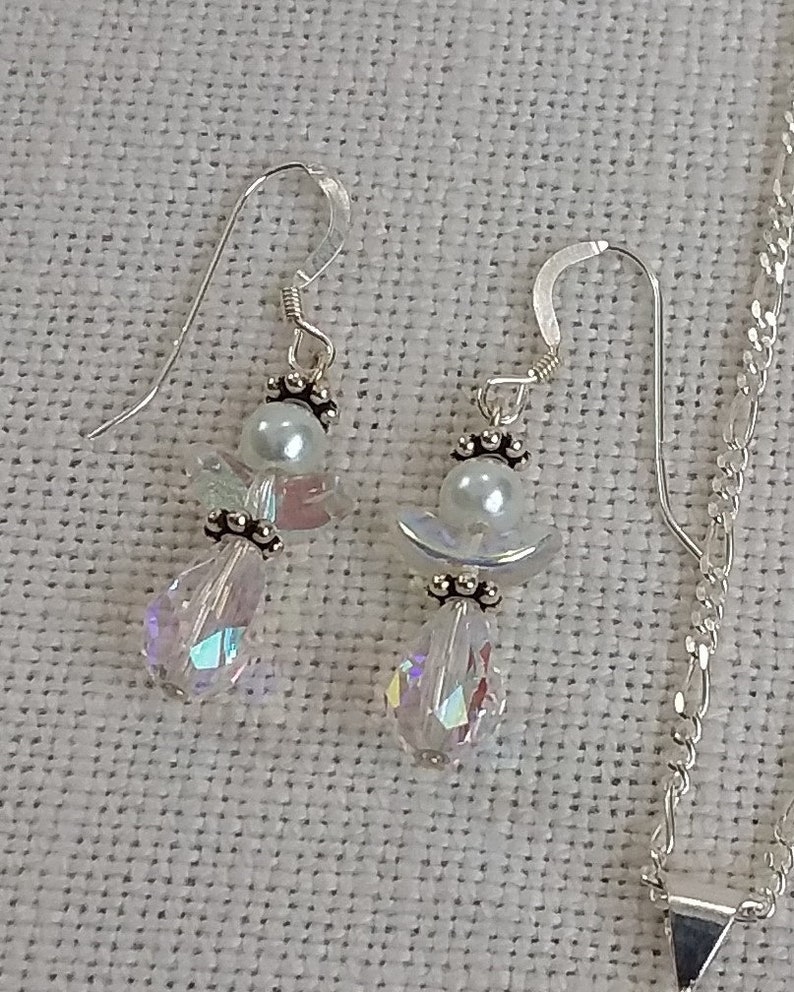 May include: A pair of silver earrings with iridescent crystal drops and white pearl accents. The earrings feature a delicate angel design.