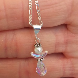 May include: A silver chain necklace with a small angel pendant. The angel is made of white beads and a clear iridescent crystal.
