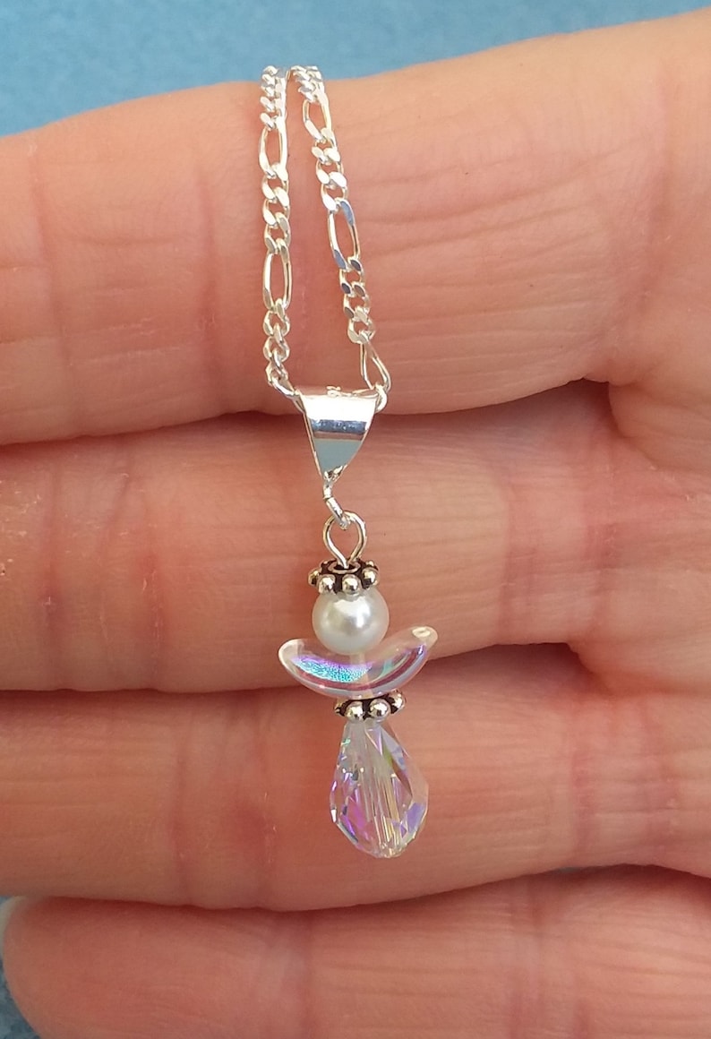 May include: A silver chain necklace with a small angel pendant. The angel is made of white beads and a clear iridescent crystal.