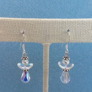May include: A pair of silver angel dangle earrings with iridescent crystal drops. The angels are made of white beads and have silver wings.