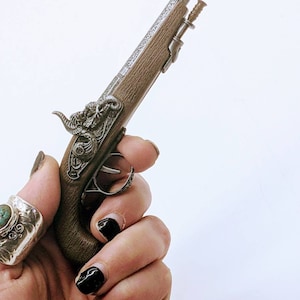 May include: A small, silver-plated pistol with a wooden grip and intricate engravings. The pistol has a decorative ram's head on the top.