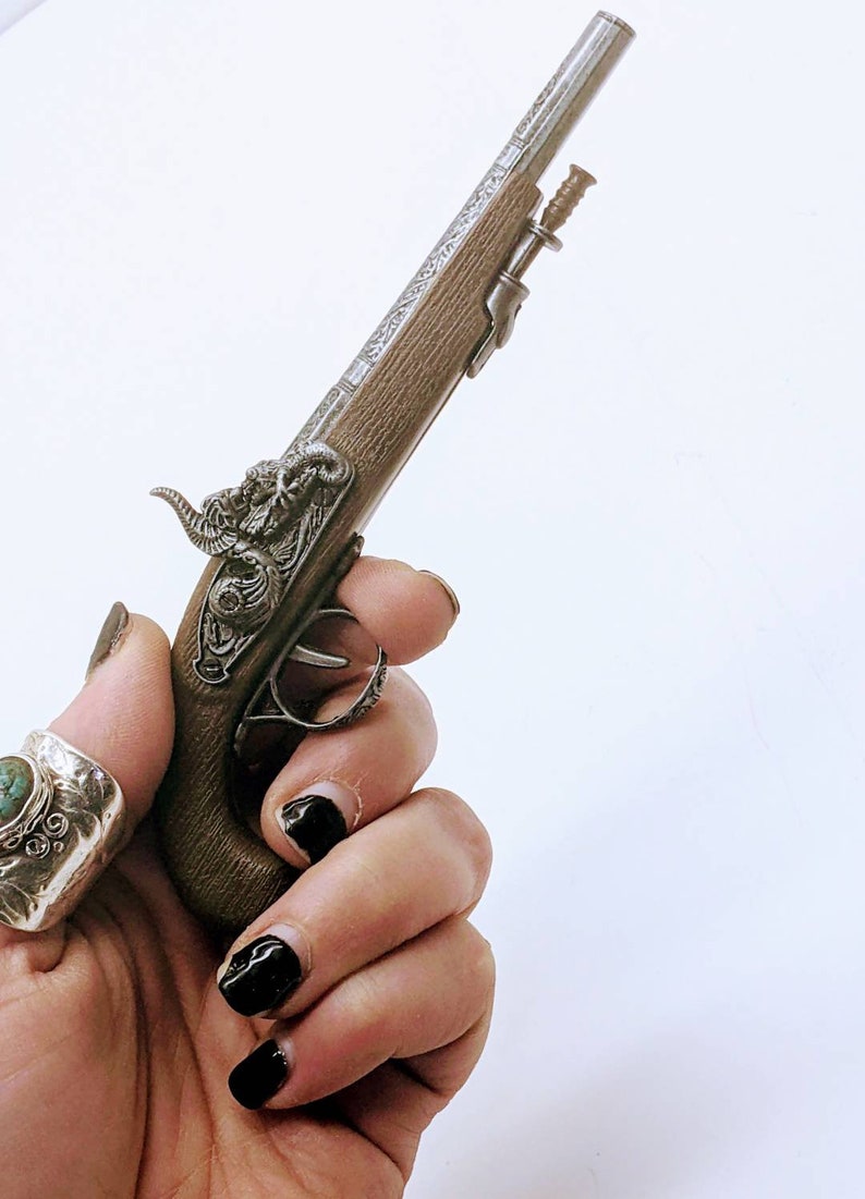 May include: A small, silver-plated pistol with a wooden grip and intricate engravings. The pistol has a decorative ram's head on the top.