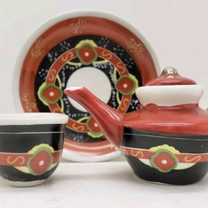 Peut inclure: Un service à thé rouge et noir avec une théière, une tasse et une soucoupe. L'ensemble présente un motif géométrique avec des accents rouges, noirs et jaunes.