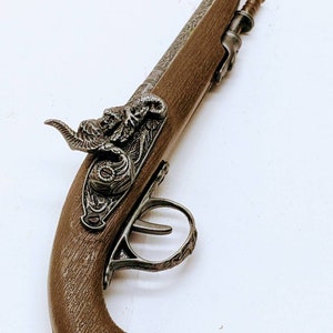 May include: A brown and silver toy pistol with a decorative design on the handle and a detailed animal head on the top.