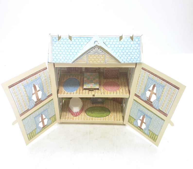 Puede incluir: Una casa de mu&ntilde;ecas de cart&oacute;n con un techo azul y amarillo y dos puertas abiertas que revelan un interior de dos pisos con muebles y alfombras.