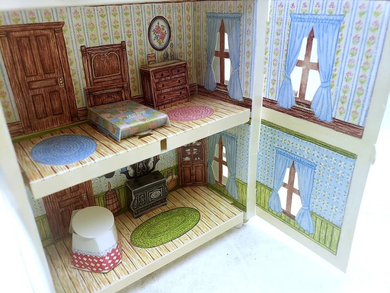 Puede incluir: Una casa de mu&ntilde;ecas en miniatura de dos pisos, con un dormitorio que incluye una cama, una c&oacute;moda y una alfombra azul. El piso inferior tiene una cocina con una estufa y un piso de cuadros rojos y blancos.