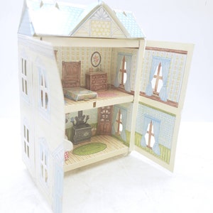 Puede incluir: Una casa de mu&ntilde;ecas de cart&oacute;n con dos habitaciones, un dormitorio y una cocina. La casa de mu&ntilde;ecas est&aacute; pintada de blanco con molduras azules y tiene un techo azul claro. La casa de mu&ntilde;ecas est&aacute; abierta y el interior est&aacute; decorado con papel tapiz y muebles.