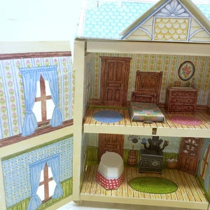 Puede incluir: Una casa de mu&ntilde;ecas de cart&oacute;n vintage con un techo azul y un exterior blanco. La casa de mu&ntilde;ecas tiene dos pisos y est&aacute; abierta para revelar las habitaciones interiores. Las habitaciones interiores est&aacute;n decoradas con papel tapiz y muebles. La casa de mu&ntilde;ecas es un gran juguete para ni&ntilde;os.