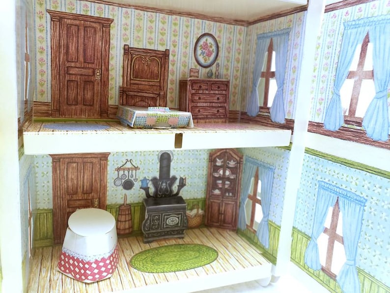 Puede incluir: Una casa de mu&ntilde;ecas en miniatura con dos habitaciones, una con una estufa de le&ntilde;a y un fregadero de cocina, y la otra con una cama y una c&oacute;moda. La casa de mu&ntilde;ecas tiene papel tapiz azul y blanco con motivos florales.
