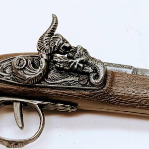May include: A silver-tone replica pistol with a wooden grip and a decorative dragon design on the top. The pistol has a detailed design and a realistic look.
