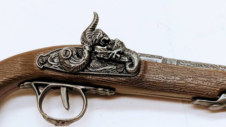 May include: A silver-tone replica pistol with a wooden grip and a decorative dragon design on the top. The pistol has a detailed design and a realistic look.
