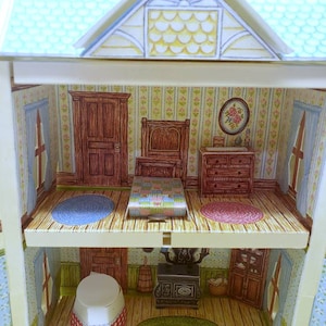 Puede incluir: Una casa de mu&ntilde;ecas en miniatura de dos pisos, con un dormitorio que incluye una cama, una c&oacute;moda y una alfombra, y una cocina con una estufa, un fregadero y gabinetes. La casa de mu&ntilde;ecas est&aacute; hecha de cart&oacute;n y tiene un techo azul.