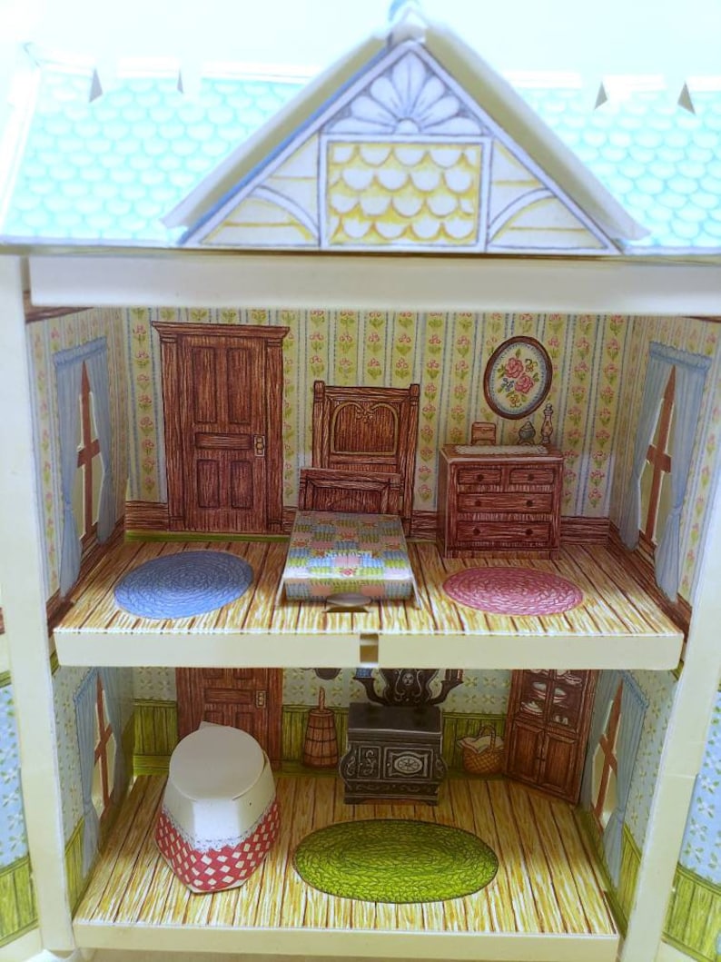 Puede incluir: Una casa de mu&ntilde;ecas en miniatura de dos pisos, con un dormitorio que incluye una cama, una c&oacute;moda y una alfombra, y una cocina con una estufa, un fregadero y gabinetes. La casa de mu&ntilde;ecas est&aacute; hecha de cart&oacute;n y tiene un techo azul.