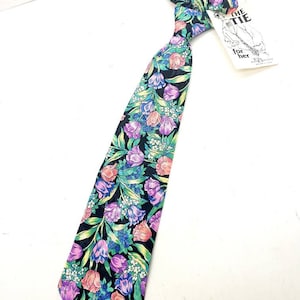 Puede incluir: Una corbata negra con un estampado floral con tulipanes rosas, morados y verdes sobre un fondo negro. La corbata tiene una etiqueta adjunta que dice "The Tie for her".