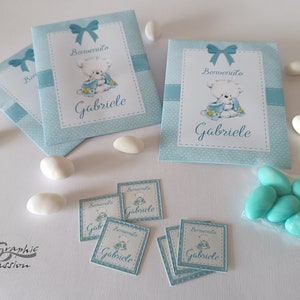 Può includere: Buste regalo blu e bianche con un disegno di orsacchiotto e il testo "Benvenuto Gabriele". Le buste sono riempite con piccoli confetti bianchi e blu. Ci sono anche piccoli adesivi quadrati con lo stesso disegno e testo.