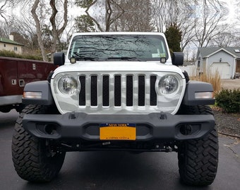 May include: White Jeep Wrangler with a camouflage pattern on the hood and a New York license plate. The Jeep has large black tires and a black front bumper.
