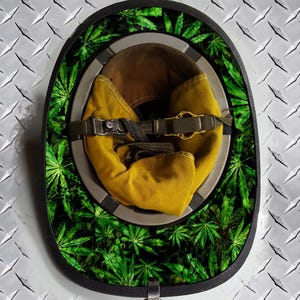 May include: A black firefighter helmet with a green and black leafy pattern around the brim. The helmet is turned upside down and the yellow liner is visible.