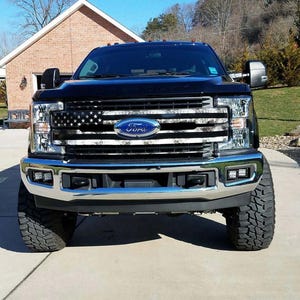 Könnte beinhalten: Schwarzer Ford F-250 Pickup mit einem Tarnmuster und einer amerikanischen Flagge auf dem Kühlergrill. Der Wagen hat große Reifen und eine Chromstoßstange.