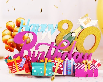Puede incluir: Una tarjeta pop-up 3D con las palabras "Happy 80th Birthday" en letras rosas, azules y doradas. La tarjeta presenta una botella de champán, globos y regalos.