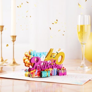 May include: A 3D pop-up card with the words "Happy 40th Birthday" in pink and gold glitter. The card features a champagne bottle, balloons, and presents.