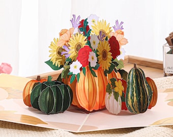 May include: A 3D pop-up card featuring a bouquet of fall flowers in a pumpkin vase. The card also includes several pumpkins and gourds.