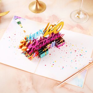 May include: A 3D pop-up birthday card with a gold "40" and the words "Happy Birthday" in pink and blue. The card is decorated with confetti and small gift boxes.