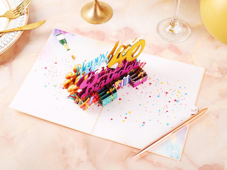 May include: A 3D pop-up birthday card with a gold "40" and the words "Happy Birthday" in pink and blue. The card is decorated with confetti and small gift boxes.
