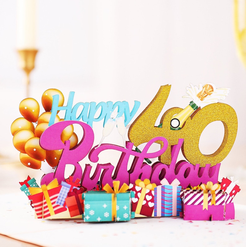 May include: A pink and gold Happy 40th Birthday cake topper with balloons, champagne, and gift boxes.