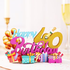 May include: A pink and gold 3D pop-up card with the words "Happy 40th Birthday" and gold balloons. The card features a champagne bottle and a gold glitter 40.