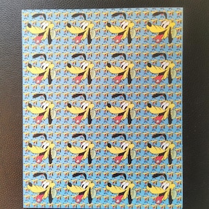 Puede incluir: Una hoja de papel con un patrón repetido de Pluto, el perro de dibujos animados de Disney. El fondo es azul claro con un patrón repetido de pequeñas estrellas y la cabeza de Pluto. Pluto es amarillo con una oreja y lengua negras.