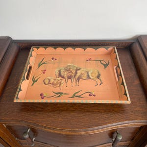 May include: A rectangular serving tray with a peach interior and scalloped edges. The tray features a painted scene of three bison and floral accents. The handles are integrated into the tray's design.