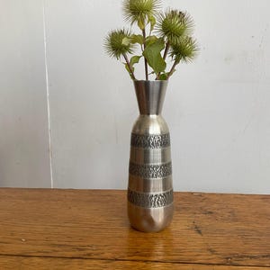 May include: A silver vase with a textured design, holding a bouquet of dried green thistle flowers.
