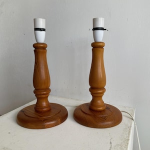 May include: Two wooden table lamps with white lampshades and black cords. The lamps have a simple, classic design.