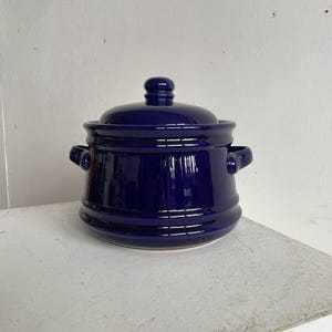 May include: A dark blue ceramic jar with a lid and two handles. The jar has a glossy finish.