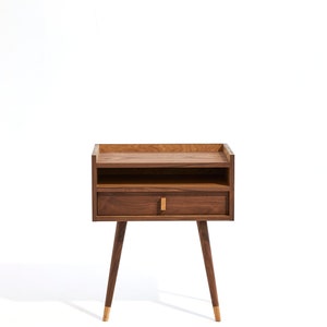 May include: A wooden nightstand with a single drawer and a shelf. The nightstand has a dark brown finish and gold-colored legs.