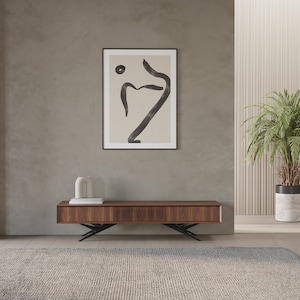 May include: A dark wood entertainment center with a slatted front and black metal legs. The center is sitting on a light gray rug in front of a beige wall with a framed abstract art print.